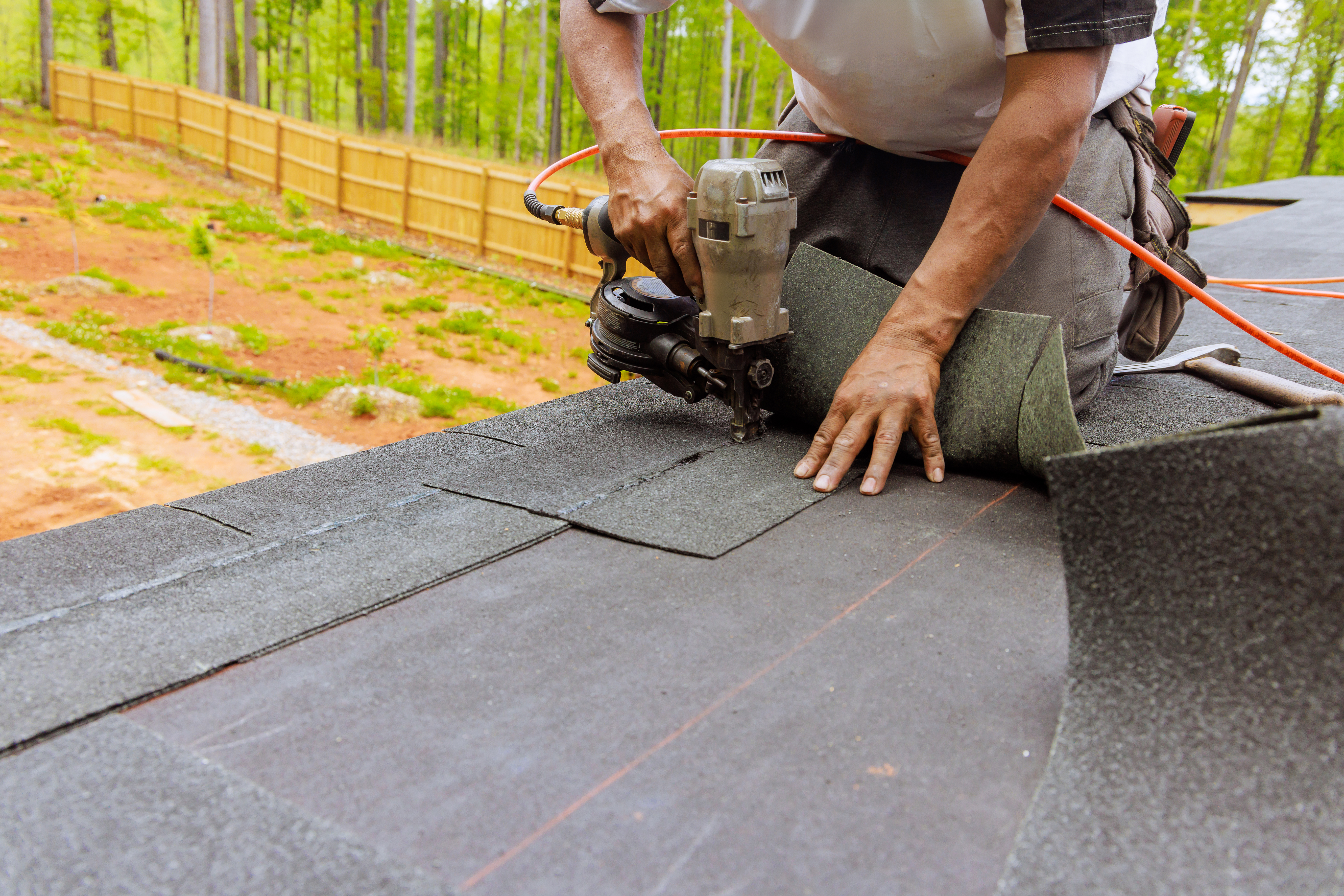 Roofer installing asphalt shingles with nail gun on residential roof